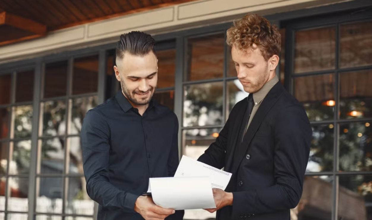 Two businessmen discussing documents at a professional meeting outdoors
