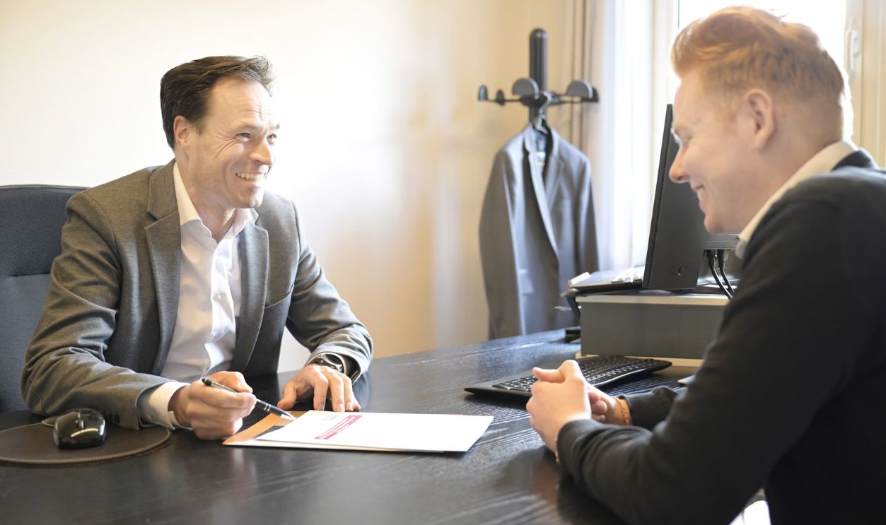 Two smiling men discussing documents at an office desk