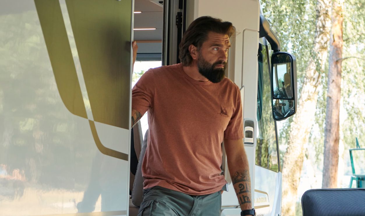 Bearded man stepping out of camper van in sunny Lithuania, showcasing outdoor adventure