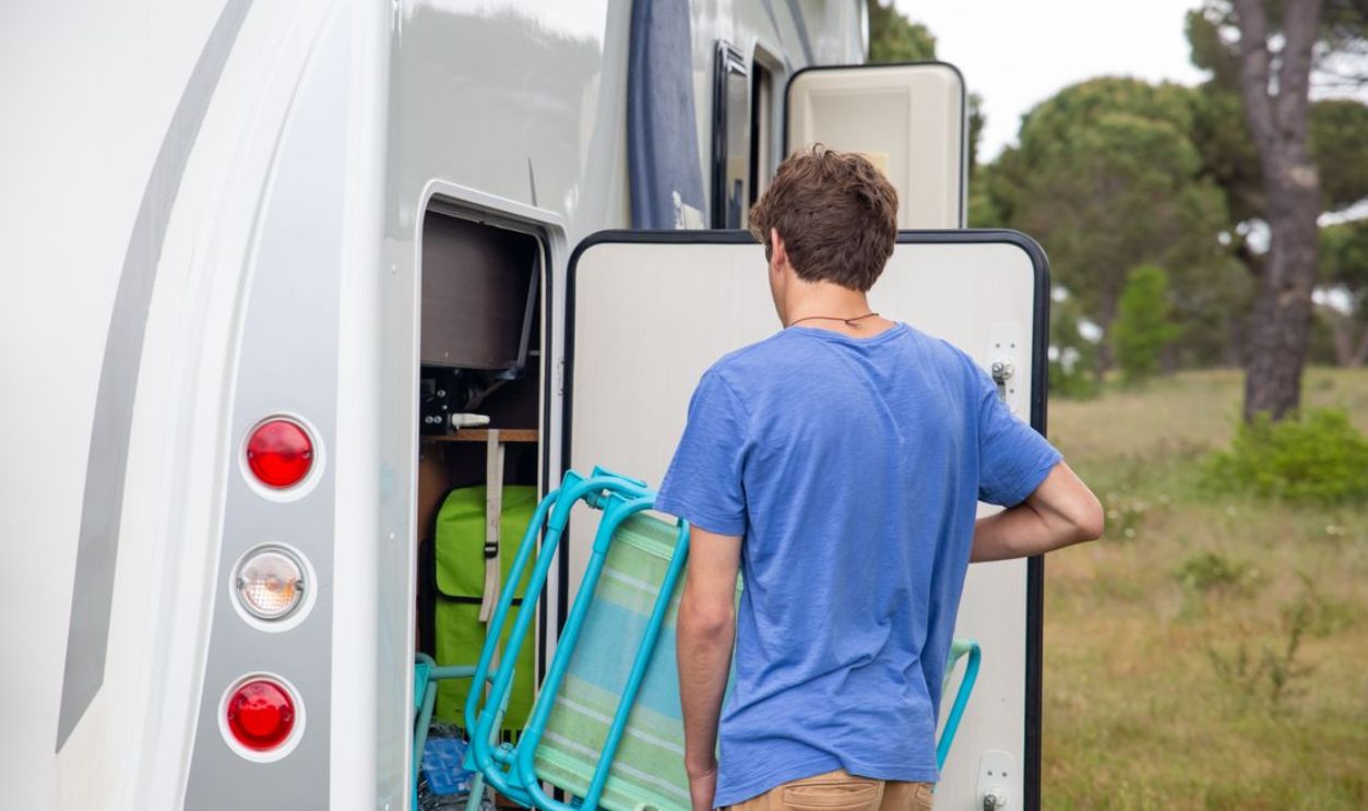 A man loads camping gear into an RV, preparing for an outdoor adventure in a lush, green environment