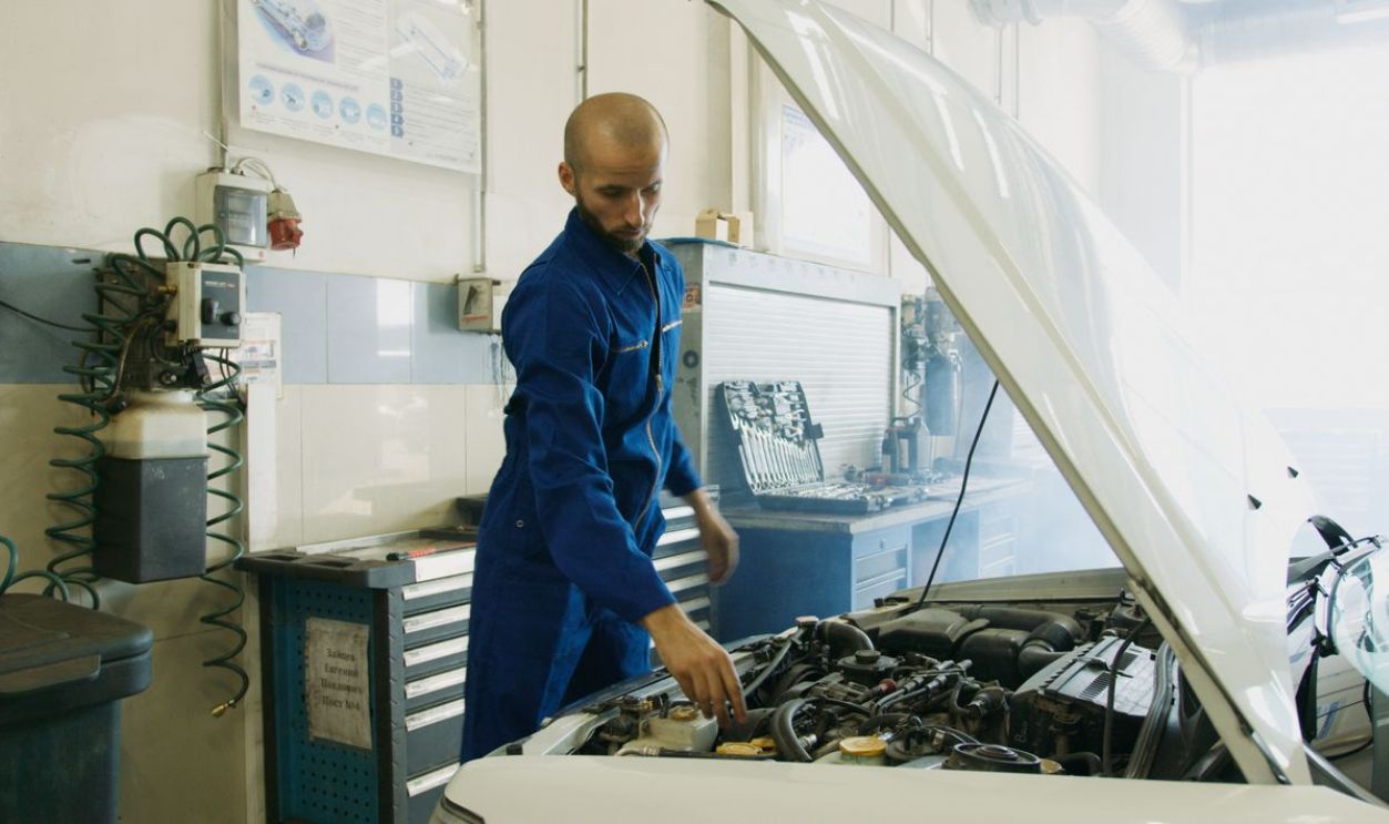 Mechanic in blue uniform inspecting a car engine in a workshop