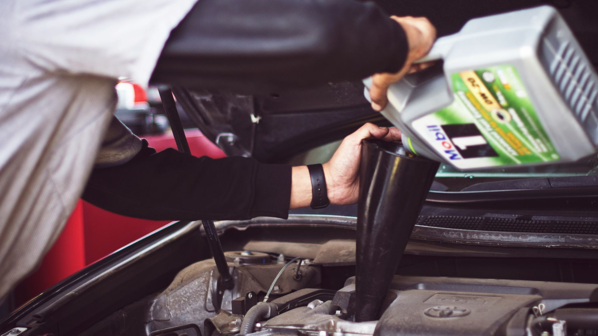 man refilling motor oil on car engine bay