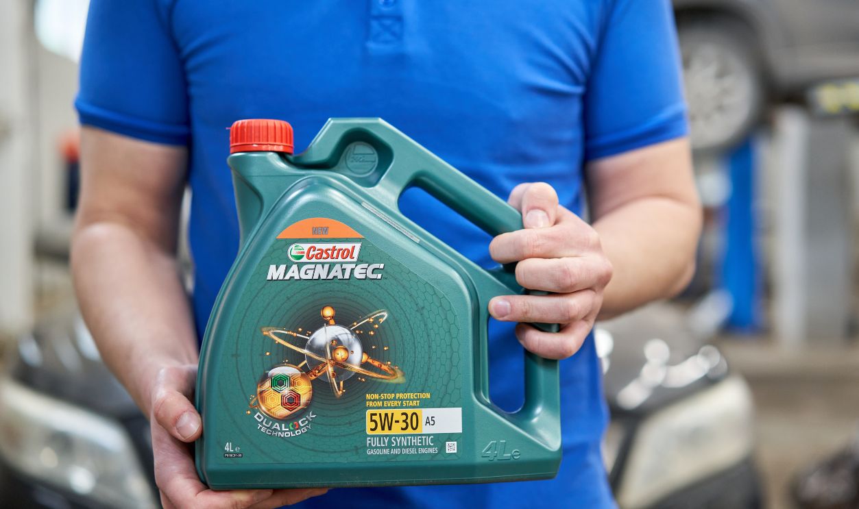Russia, Nizhny Novgorod - march 13, 2020: Best way Auto service. Castrol Magnatec engine oil 5w-30. Man auto mechanic in blue uniform holding bottle at the car service. Replacing and pouring fresh oil