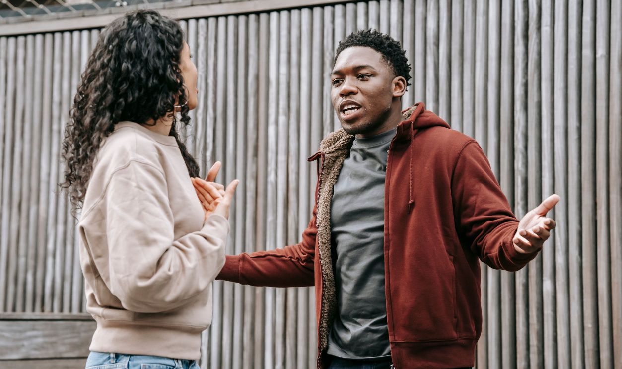 A couple having an argument outside against a wooden fence.