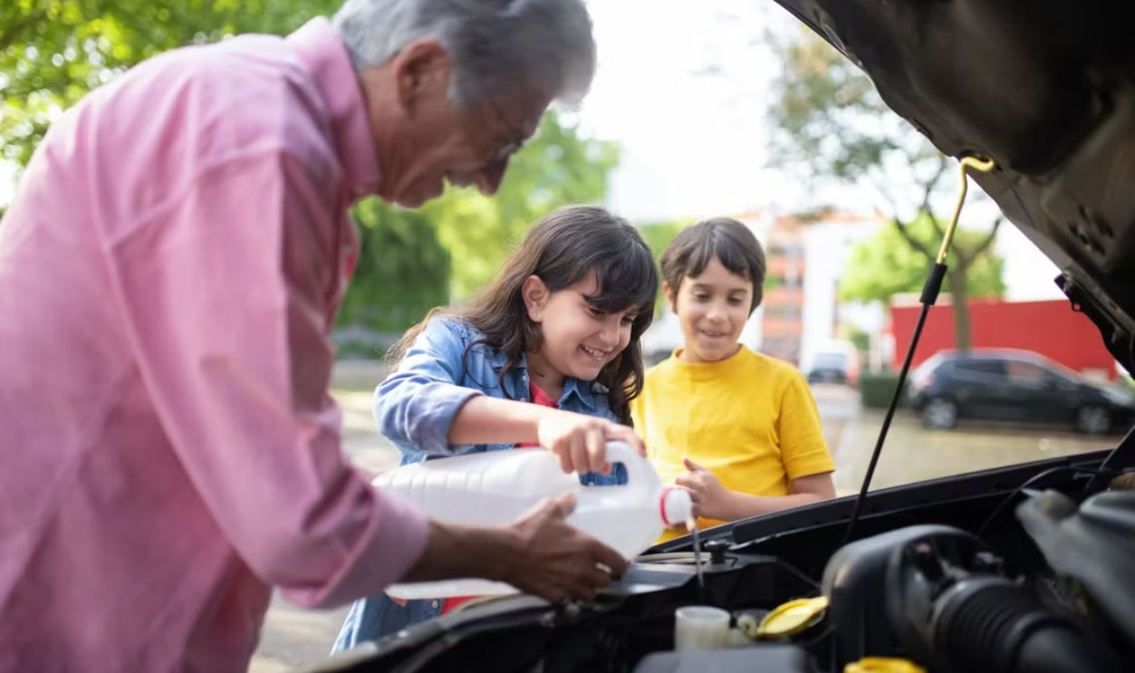 A grandfather and his grandchildren refilling car windshield fluid on a sunny day outdoors.