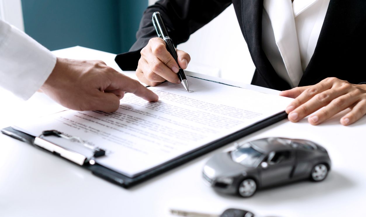 Closeup of Asian female signing car insurance document or lease paper contract or agreement. Buying or selling new or used vehicle with car keys on table.