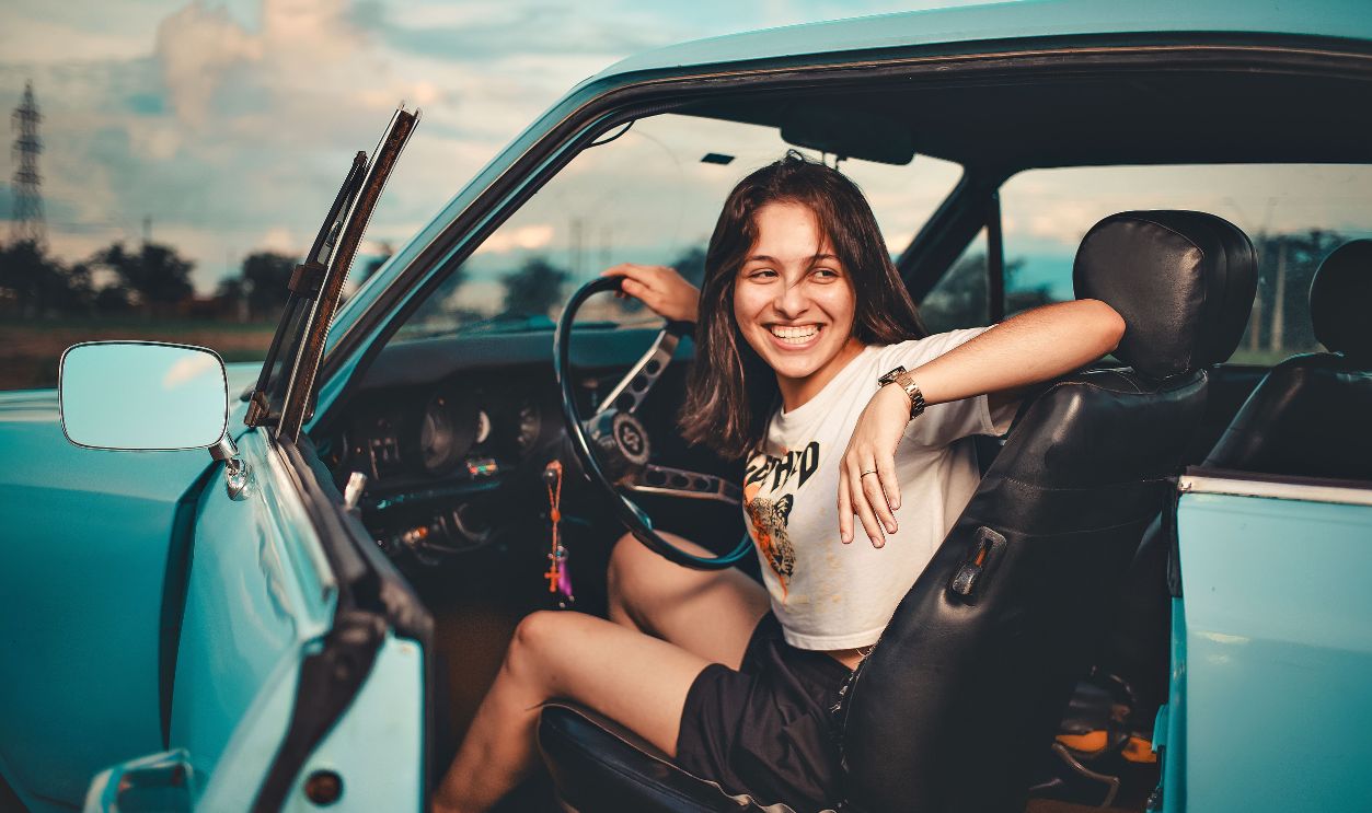 A cheerful young woman sitting in a blue vintage convertible car