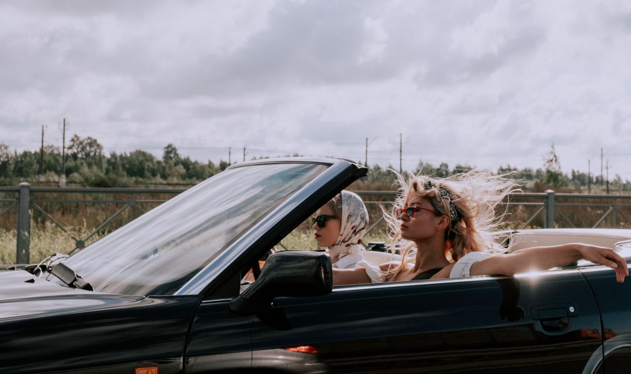 Two fashionable women driving a convertible with sunglasses