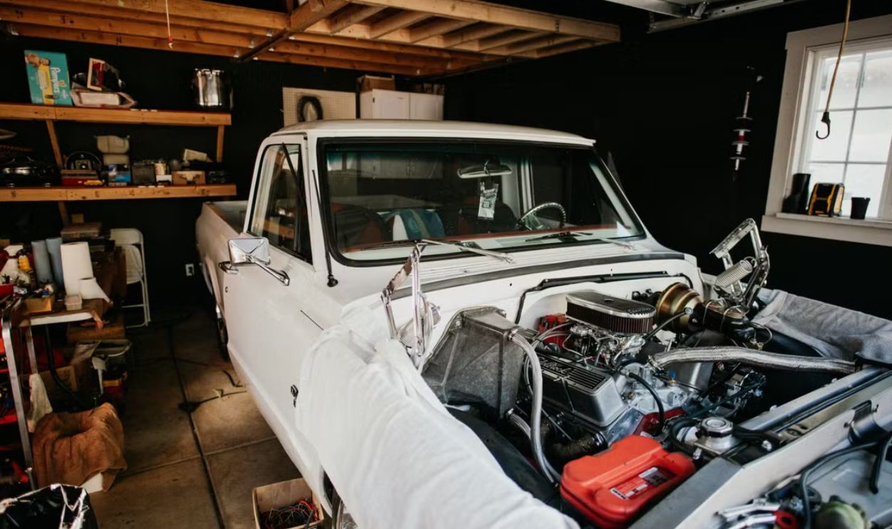 A vintage pickup truck undergoing engine repairs in a well-equipped home garage.