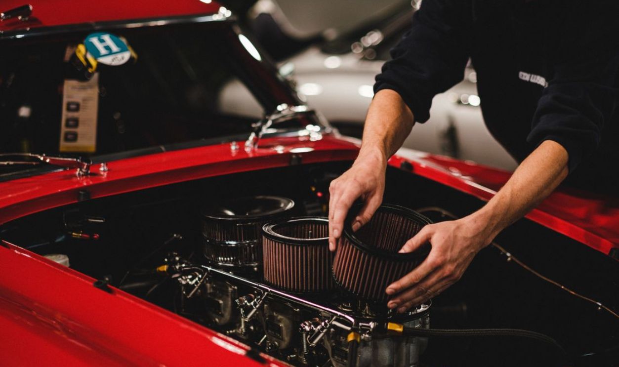 Close-up of a mechanic working on a car engine in a garage setting, focusing on air filter adjustment.