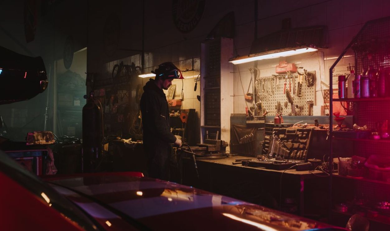 Mechanic working in a dimly lit garage workshop surrounded by tools and equipment.