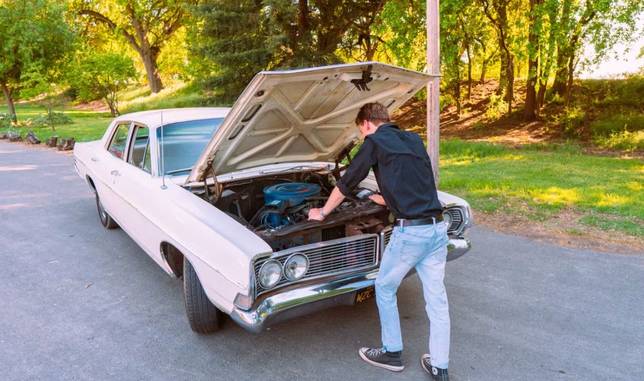 A man fixing a vintage car engine outdoors in Clarksburg, California, on a sunny day.