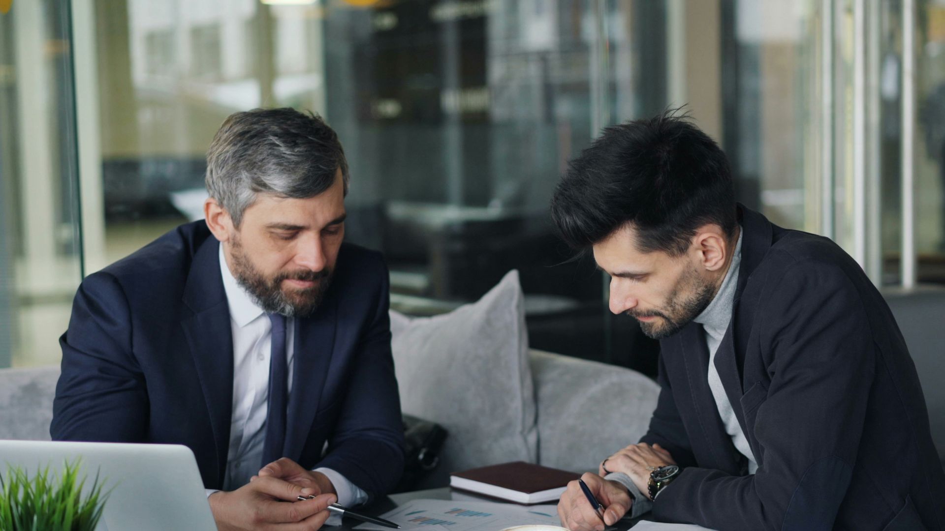 two men sitting at a table working on a laptop