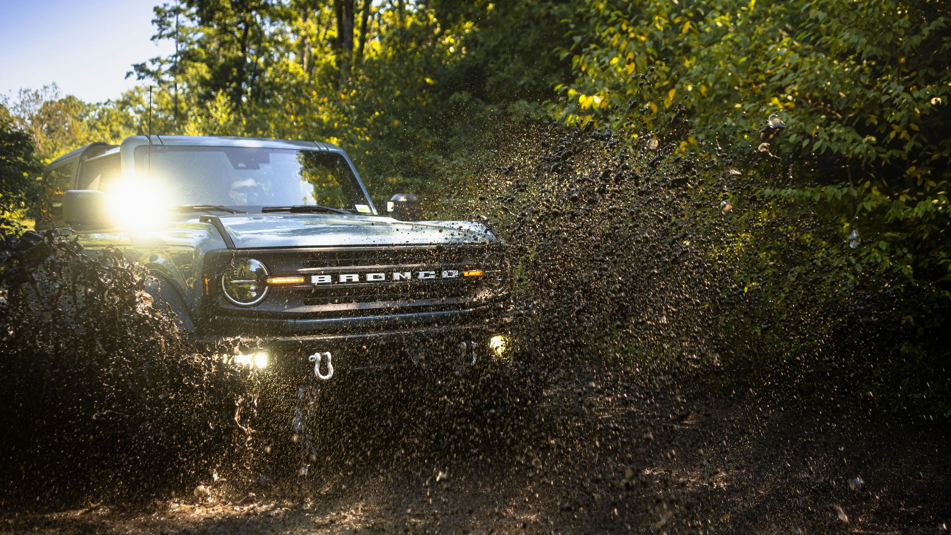 A bronco kicks up mud off-roading.