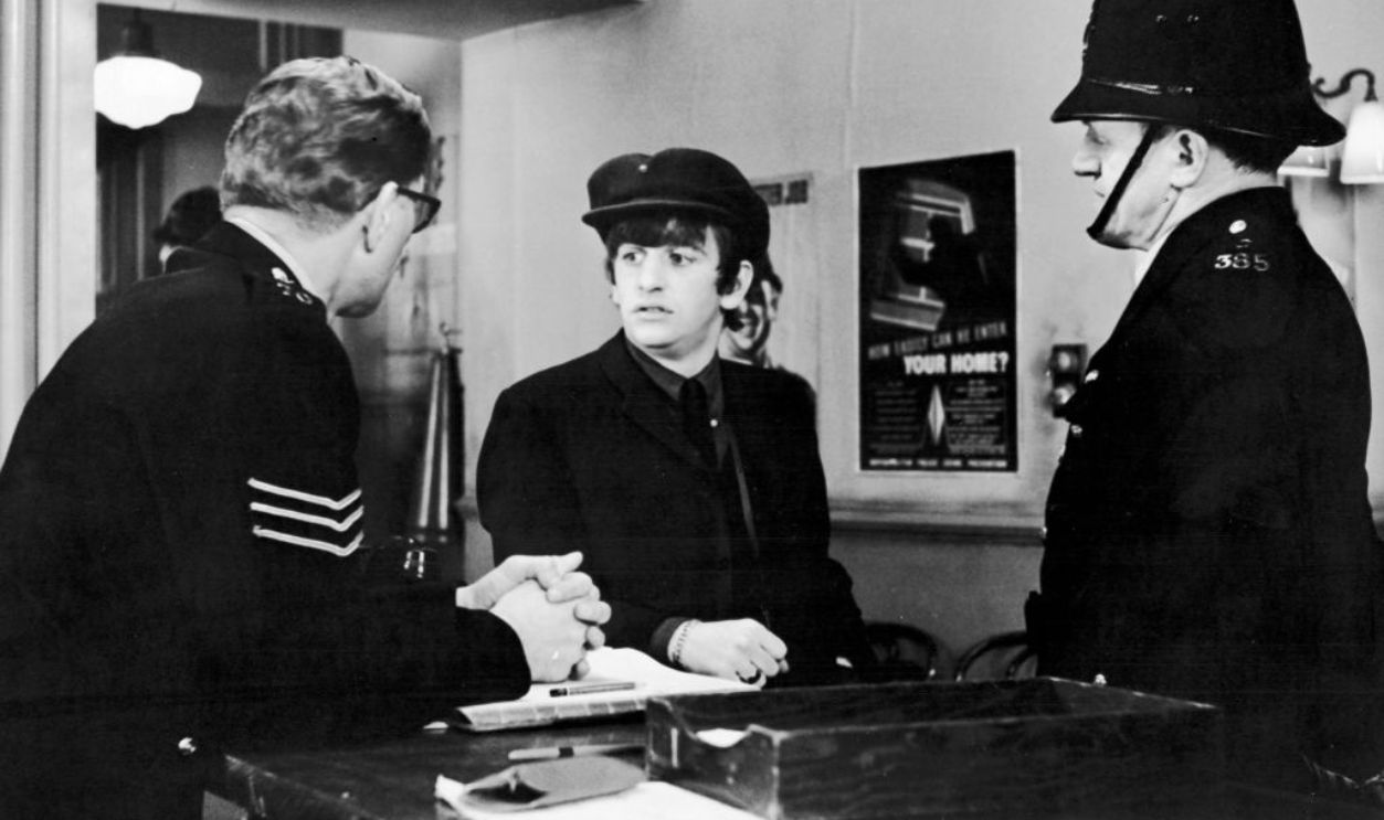 British musician Ringo Starr, of the pop group The Beatles, talks with police in a still from the film 'A Hard Day's Night,' directed by Richard Lester, 1964.