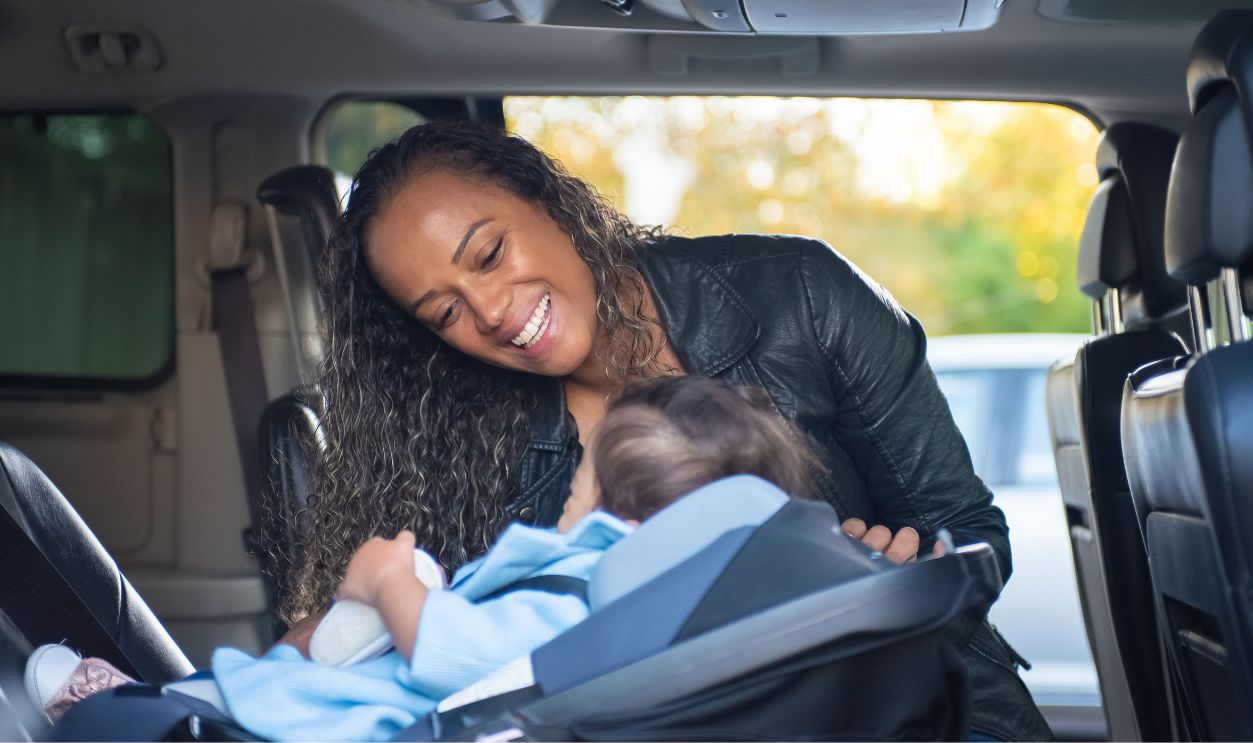 A joyful mother smiles at her baby in a car seat