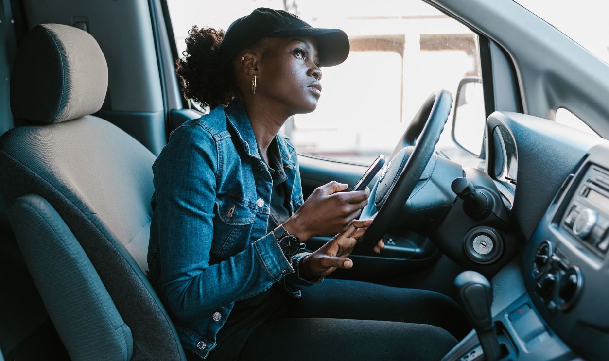 A woman in a denim jacket focuses on her smartphone while sitting in a car 