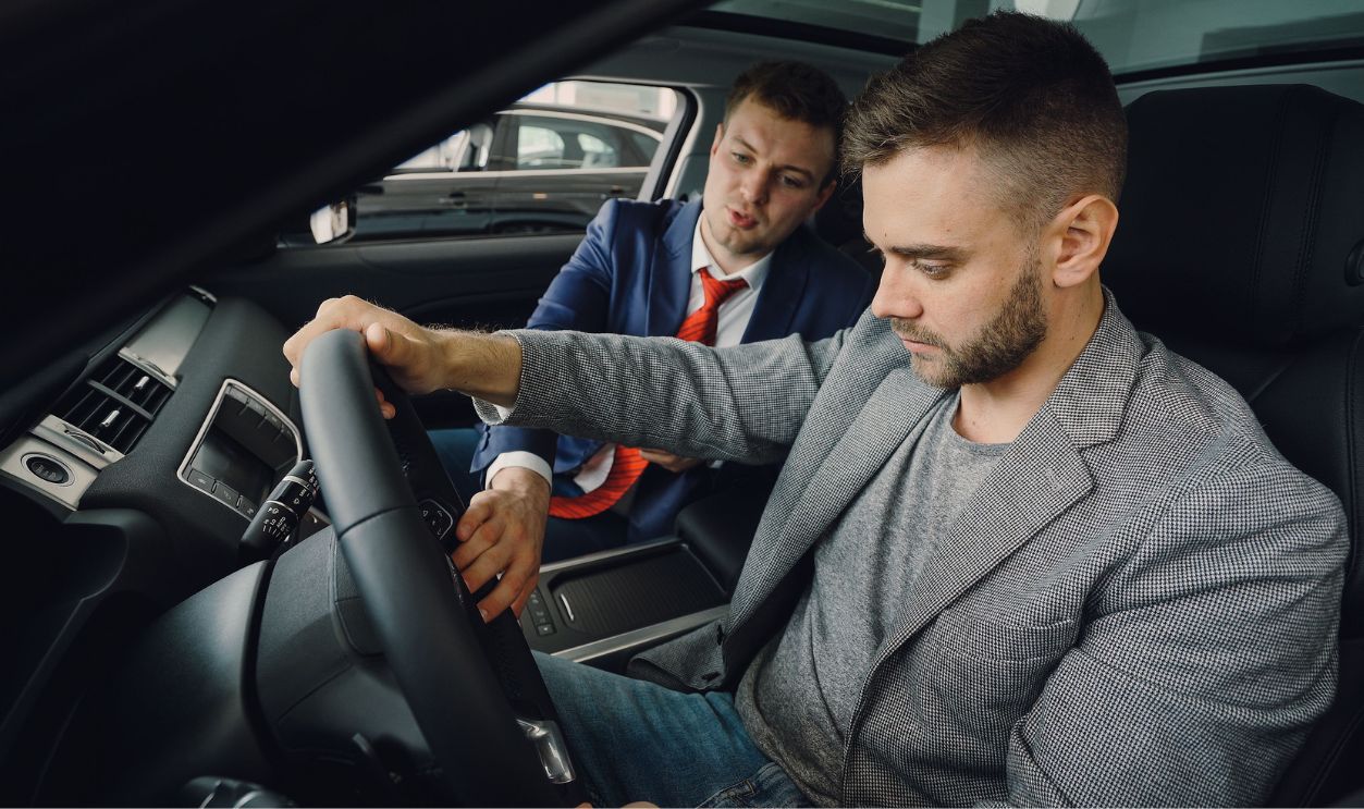 Salesman demonstrating car features to potential buyer inside vehicle