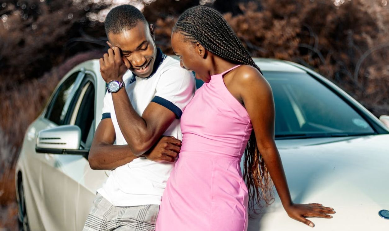 Cheerful couple leaning on a car, enjoying a sunny day outdoors.