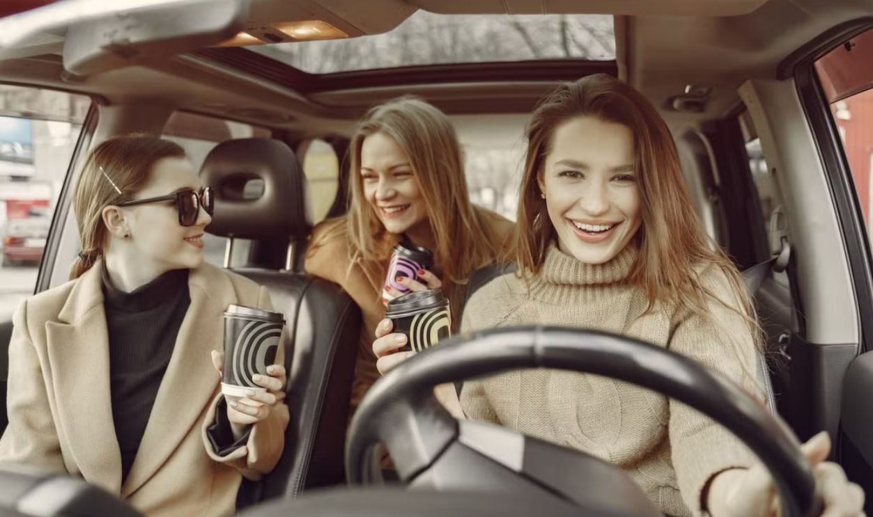 Happy friends relaxing with takeaway coffee in a car, sharing laughter and enjoyment on a casual day out.