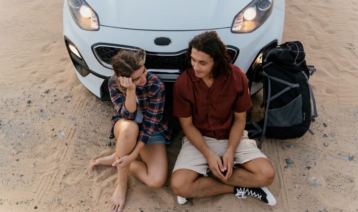 An adventurous couple sitting by a car in a sandy desert, perfect for travel themes.