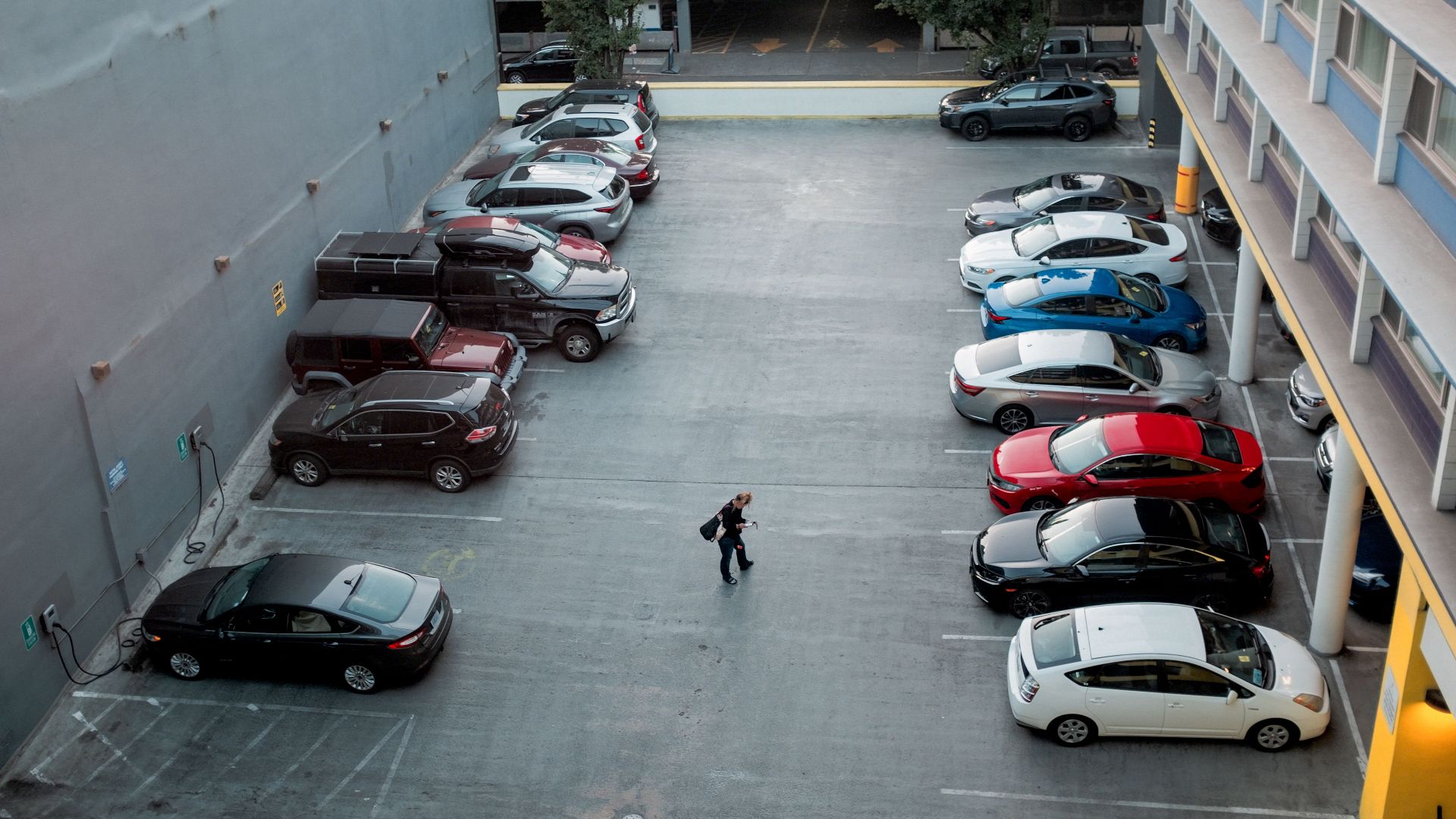 A man walks in a city parking lot filled with various cars, offering a busy urban scene.