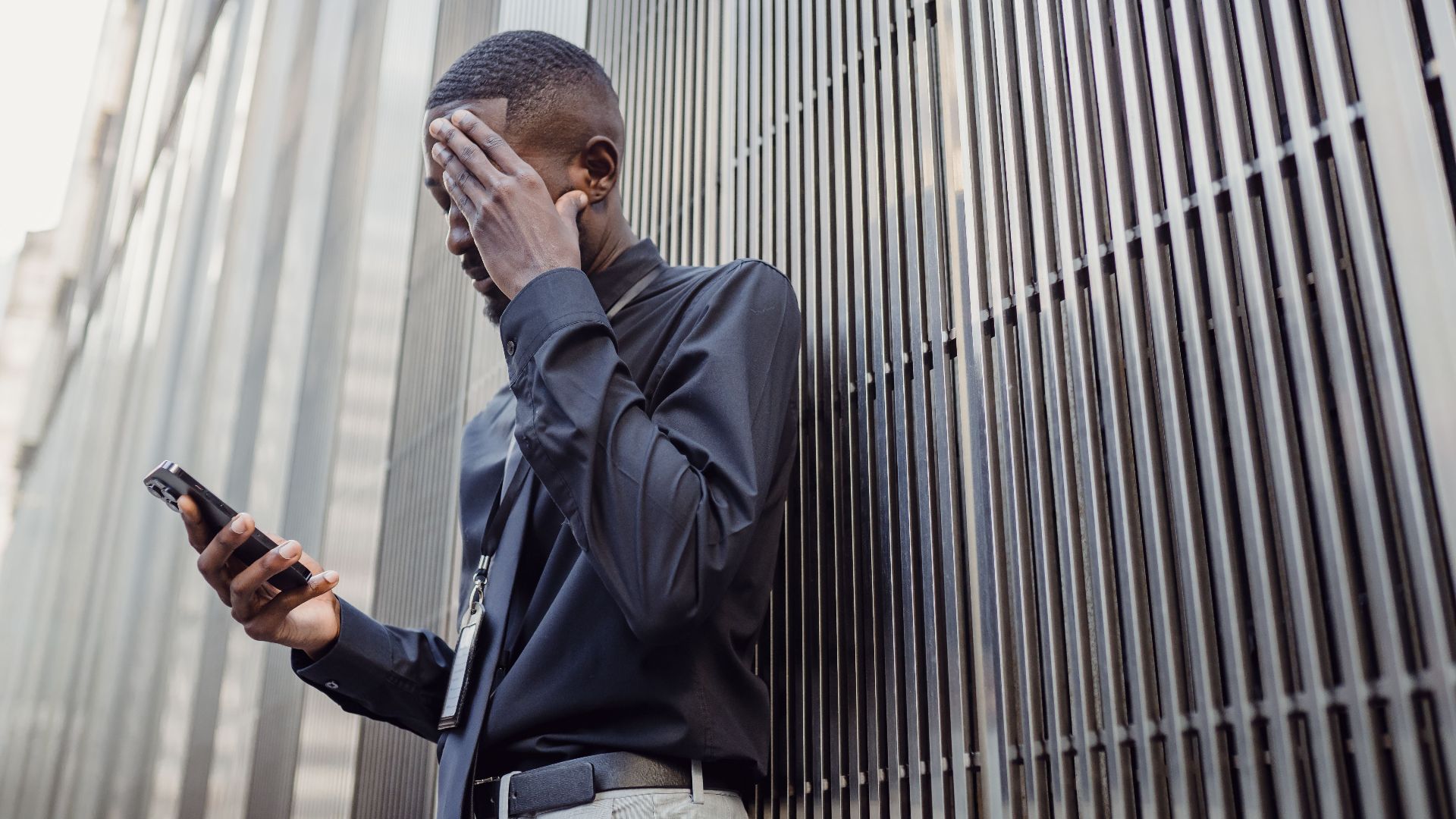 A worried businessman in formal attire using a smartphone outside a modern building.