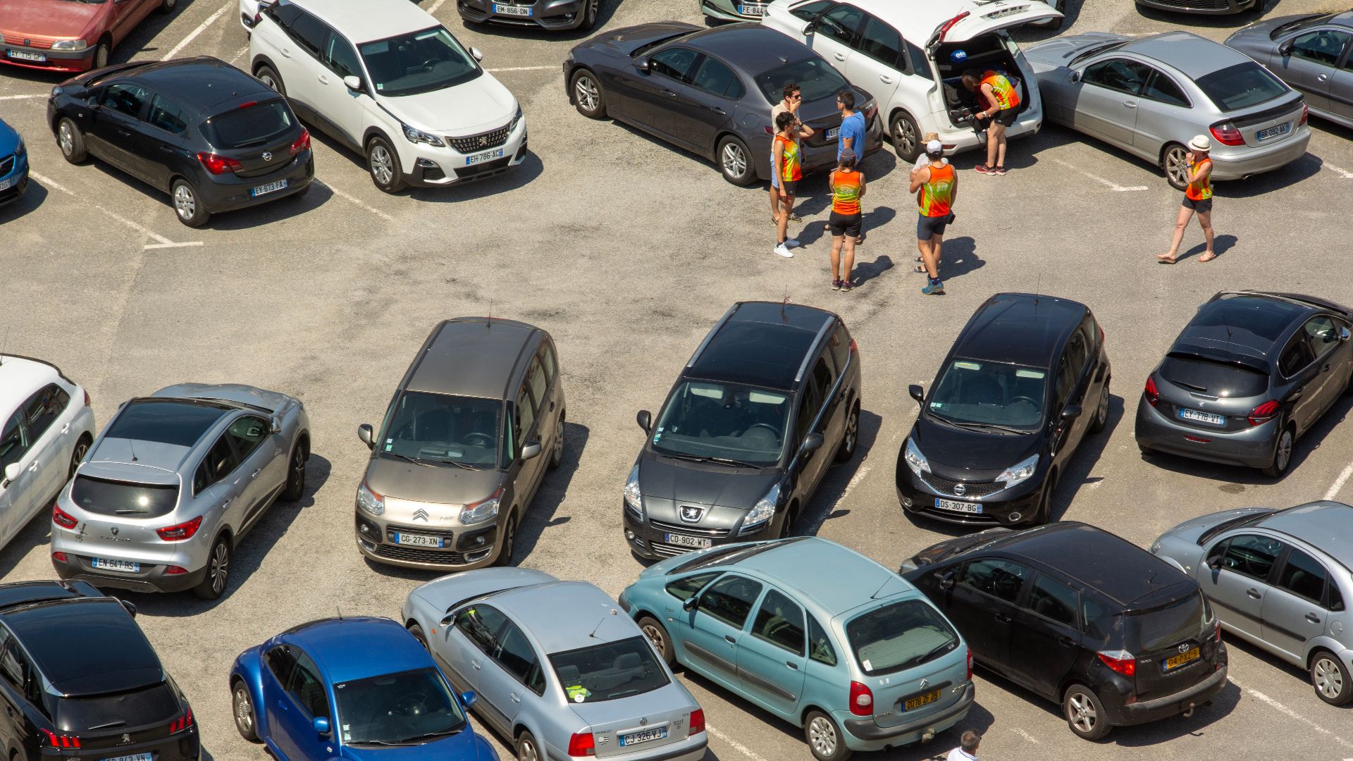 Aerial view of a crowded parking lot with various cars and people congregating.