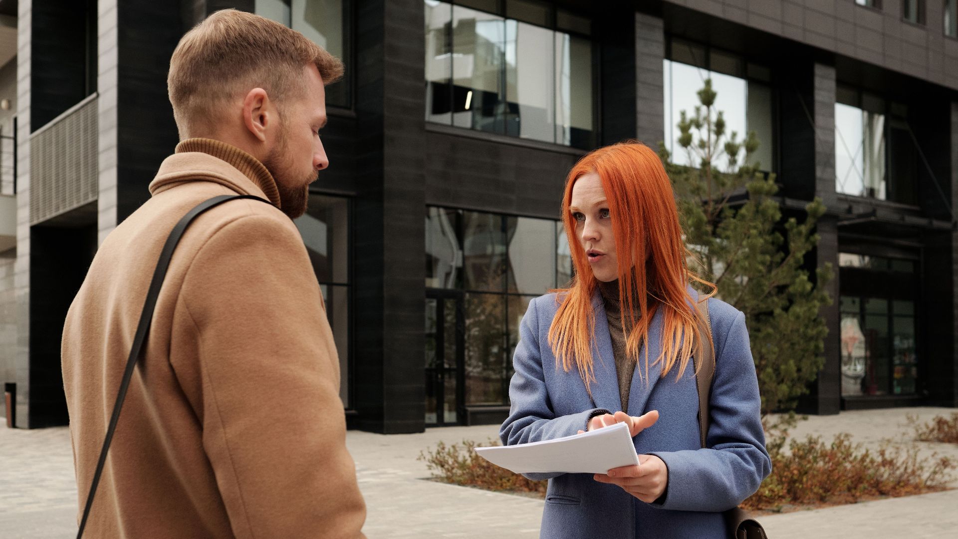 Two stylish business professionals discuss outside a modern office building.
