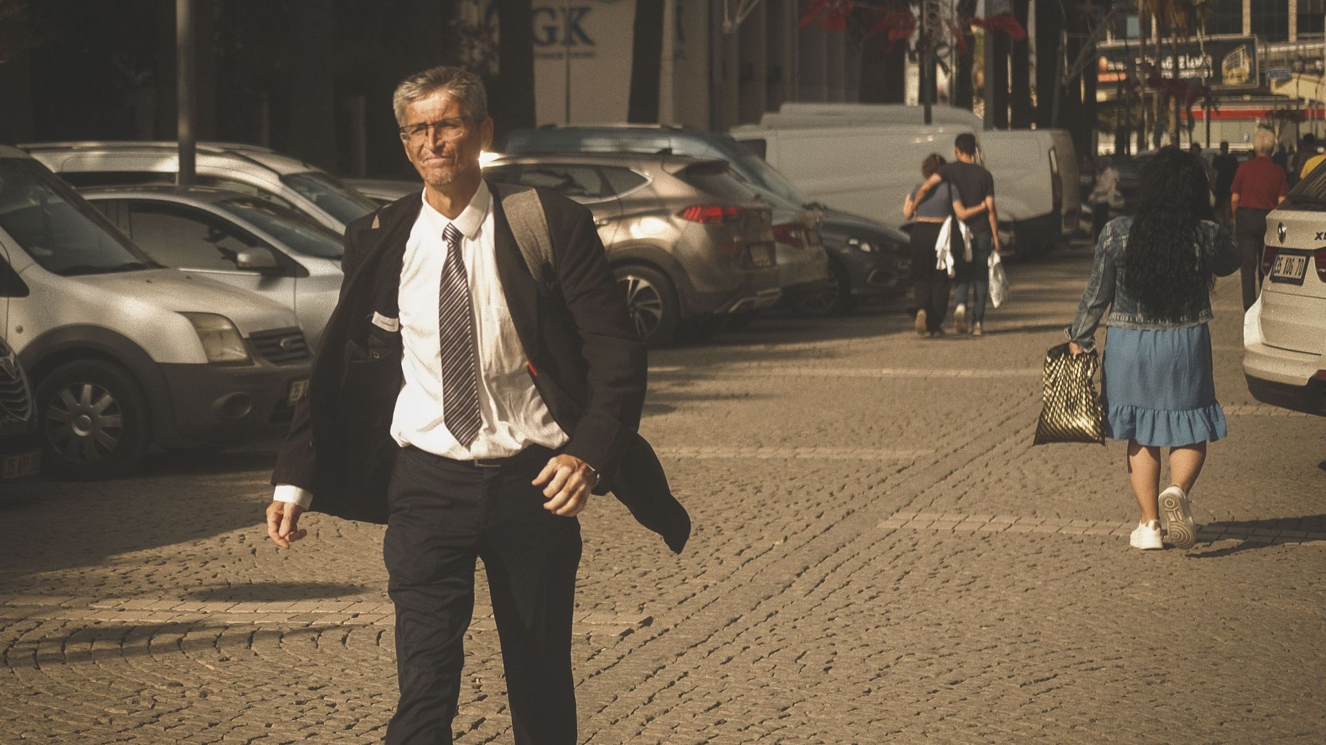 Senior man in suit confidently walks down a sunny city street.