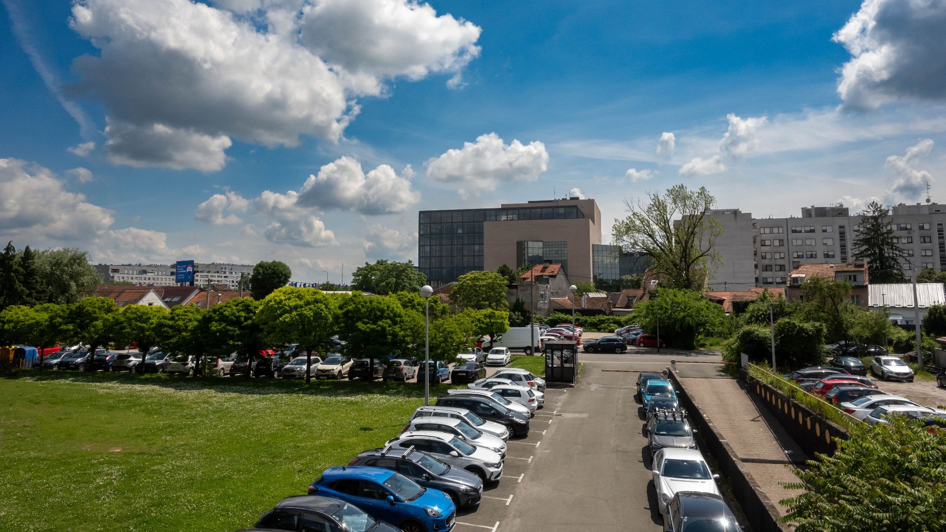 A vibrant view of an urban parking lot with fluffy clouds and city buildings in Zagreb, Croatia.