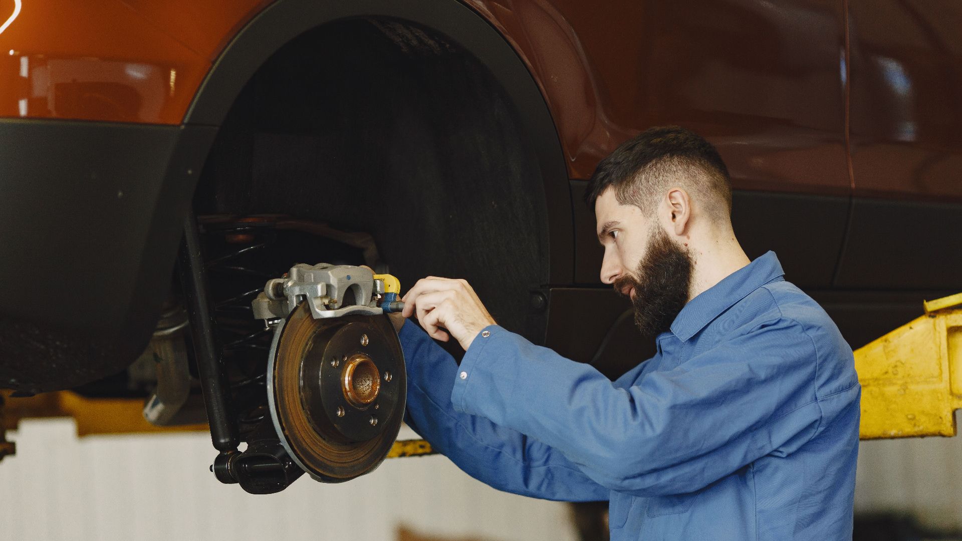 Mechanic in blue uniform performing brake repair on car in modern garage.