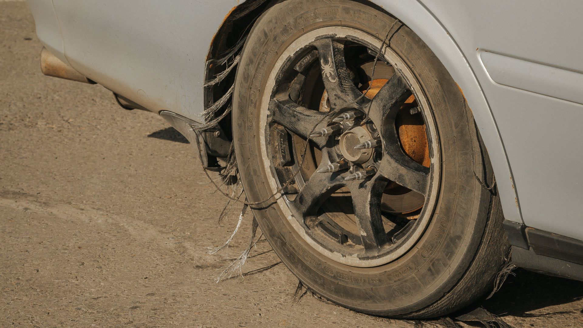 Close-up of a blue car with a severely damaged tire on weathered concrete.