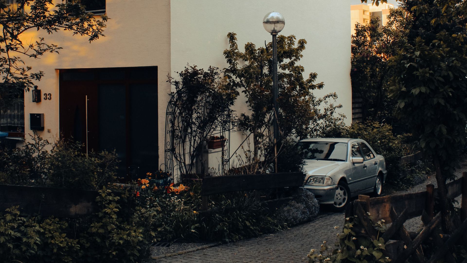 Cozy residential house with a parked car and lush garden under warm evening light.