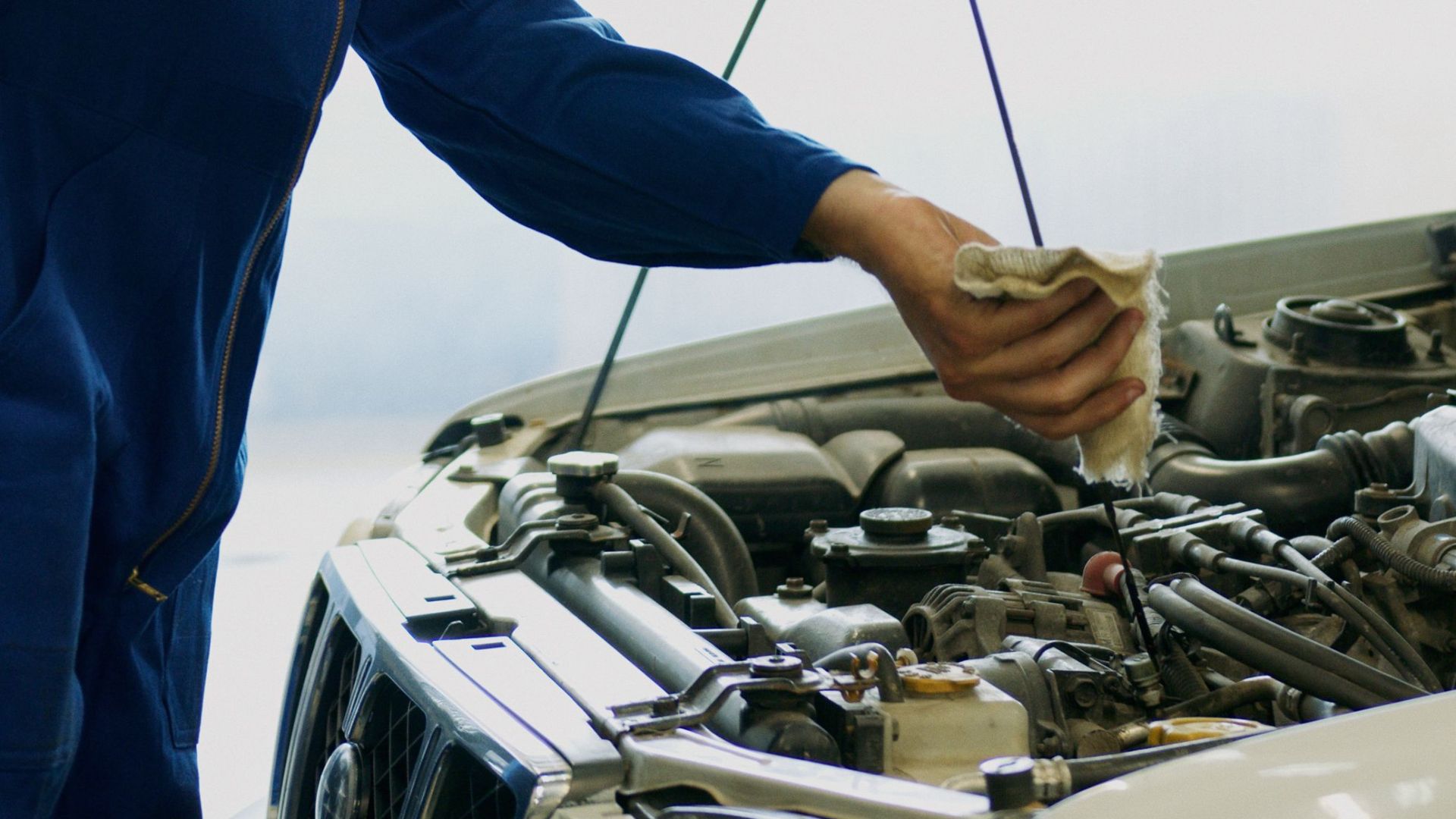 Mechanic inspecting car engine oil with dipstick in an automotive repair shop.