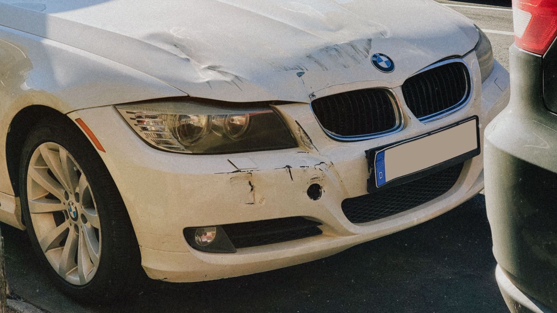 White BMW sedan with front-end damage parked on a busy city street.