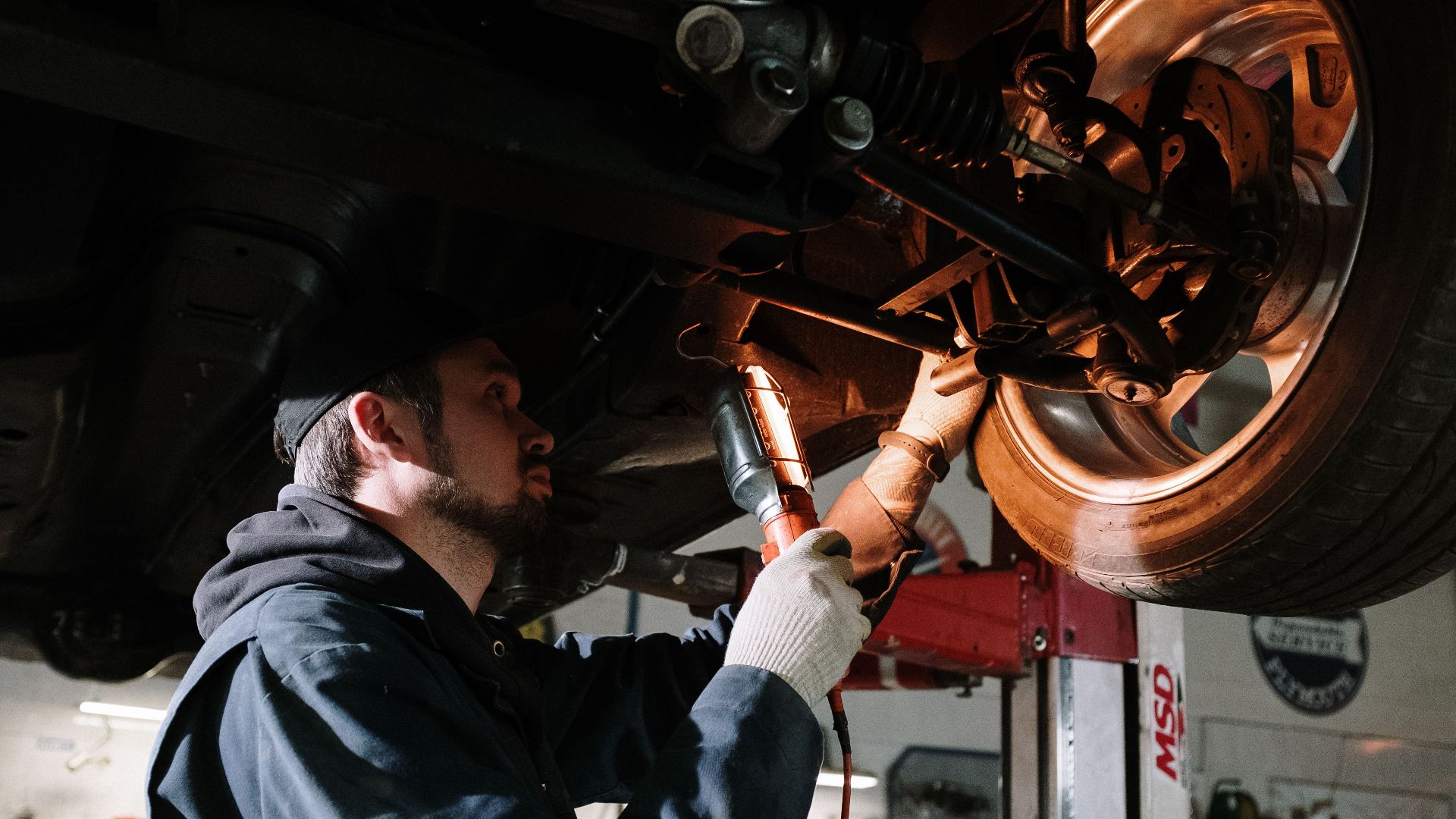 Mechanic examining car's undercarriage at a garage, focusing on vehicle maintenance.