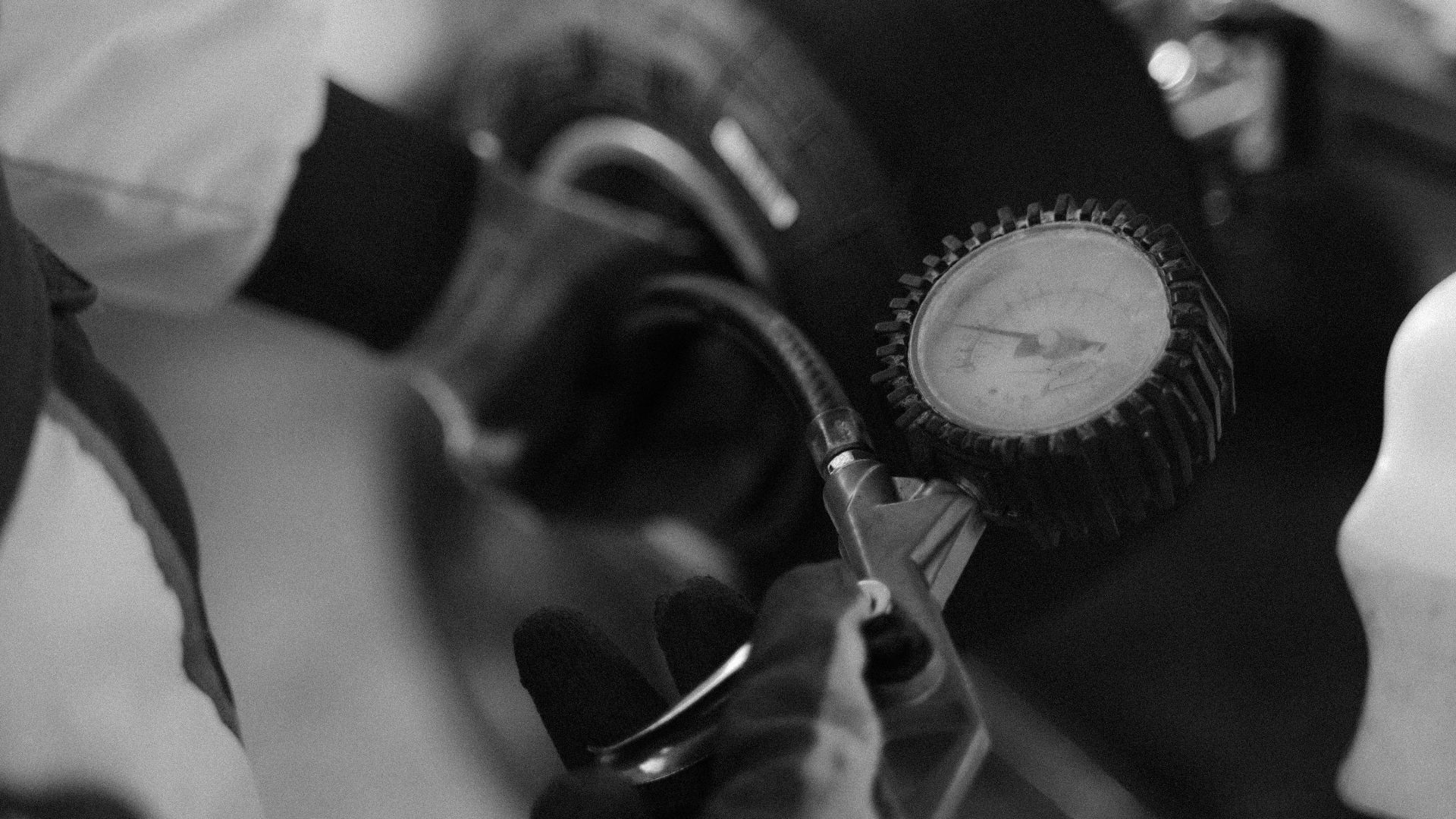 Black and white image of a mechanic using a gauge to check tire pressure on a kart wheel.