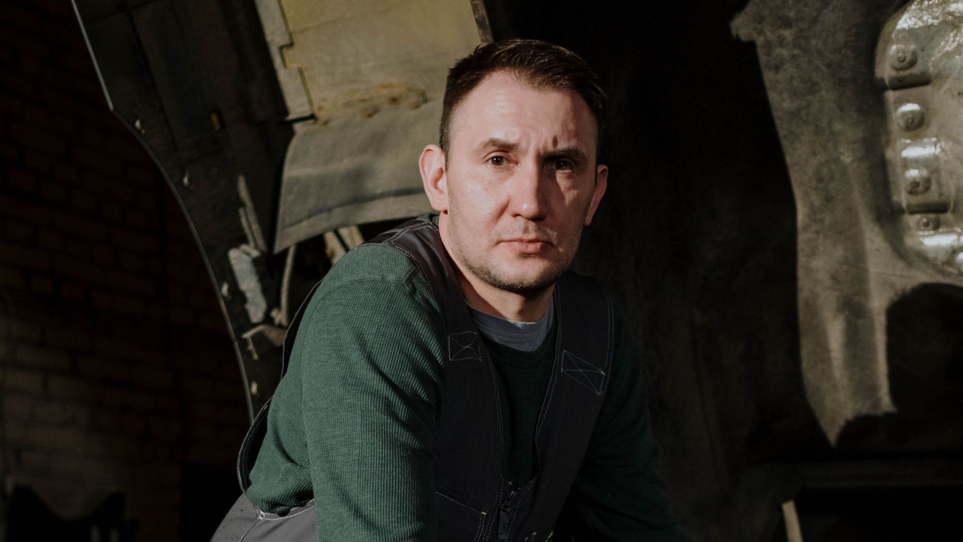 A male mechanic leaning over a car engine in a workshop, focused on repairs.