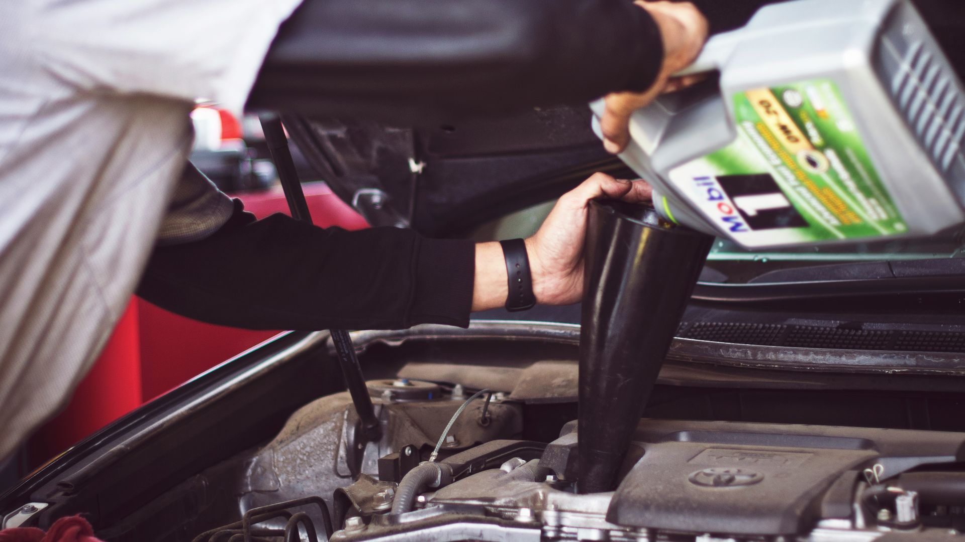 man refilling motor oil on car engine bay