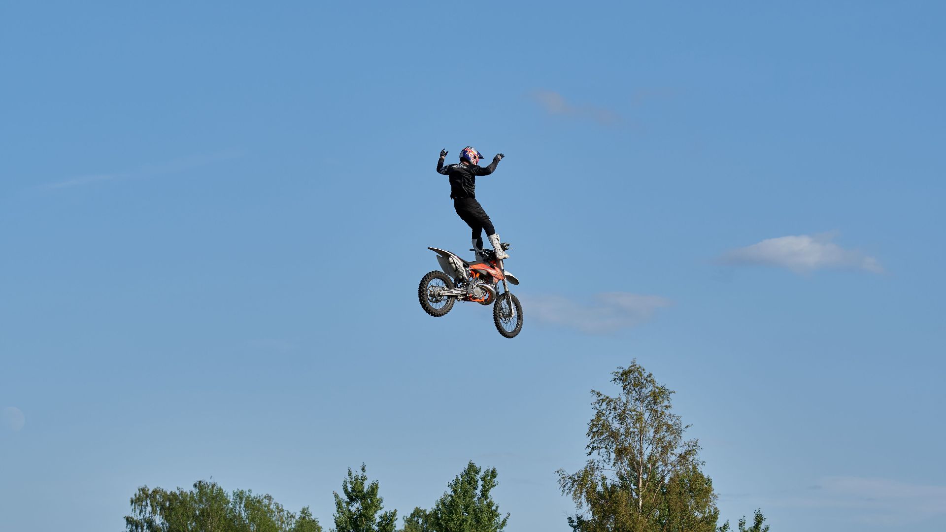 Exciting motocross stunt with rider mid-air against a bright blue sky.
