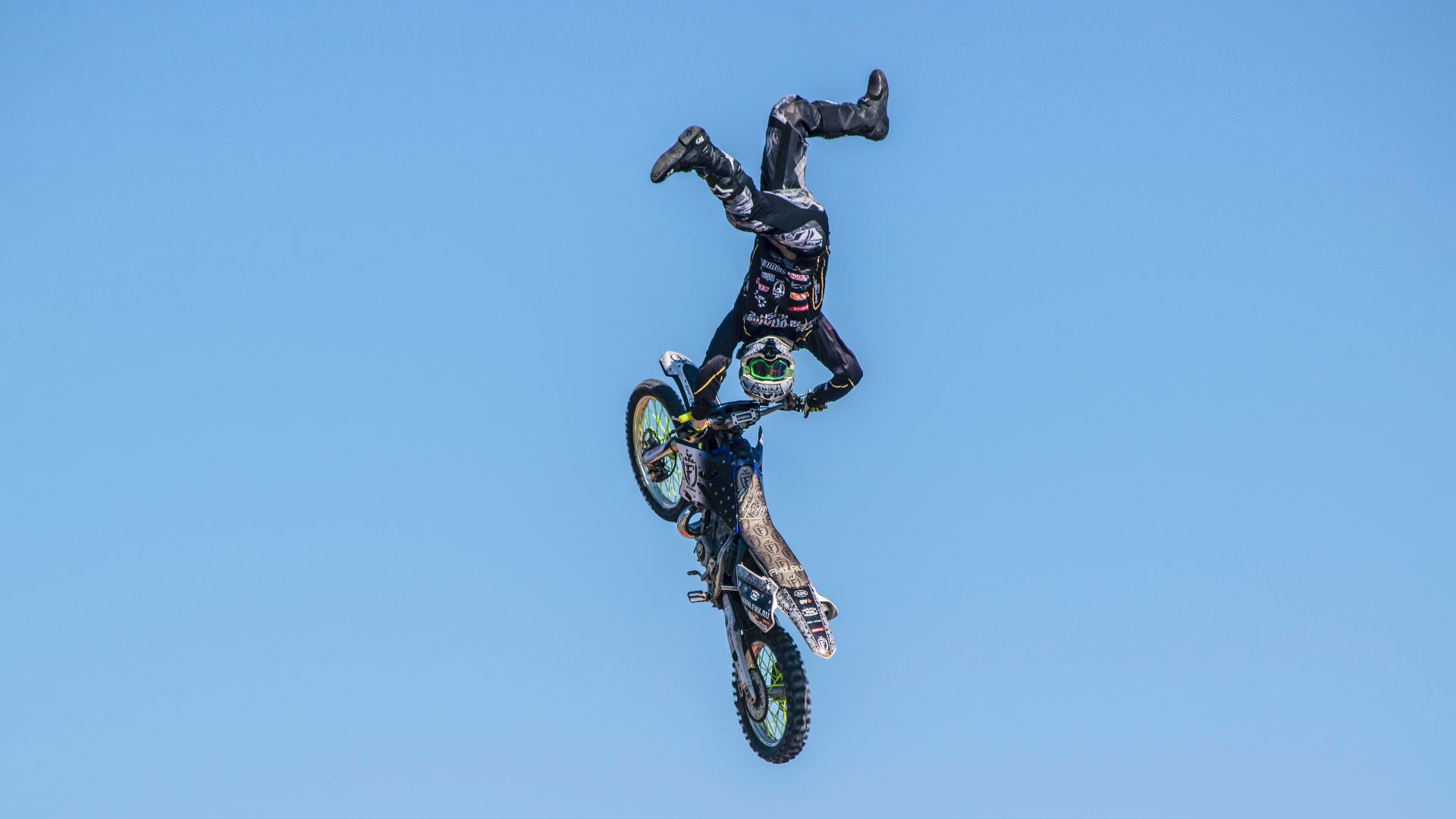 Daring motocross stunt captured mid-air against a clear blue sky.