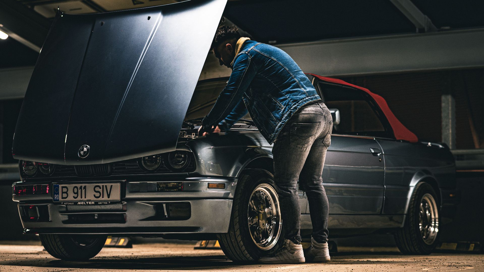 Man working on a convertible car in a garage, checking the engine under the hood.