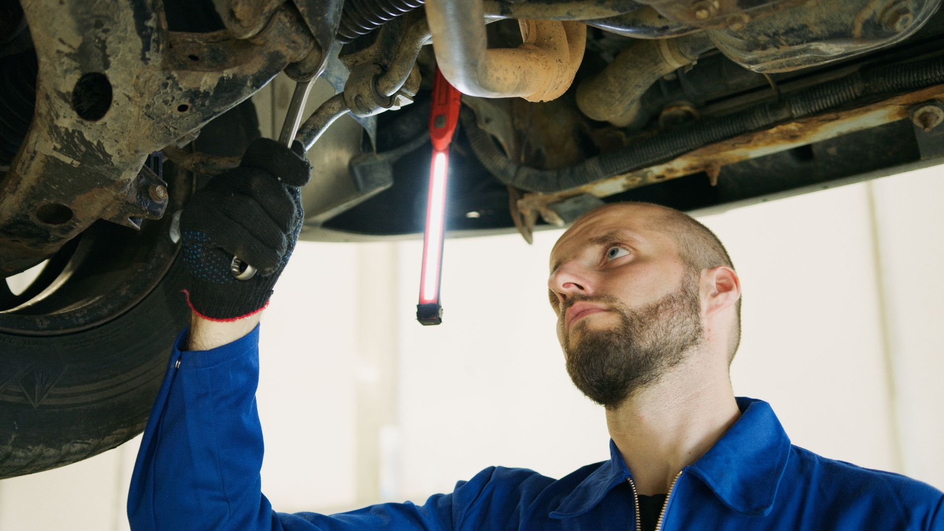 Mechanic focusing on vehicle maintenance under a car lift in a garage.