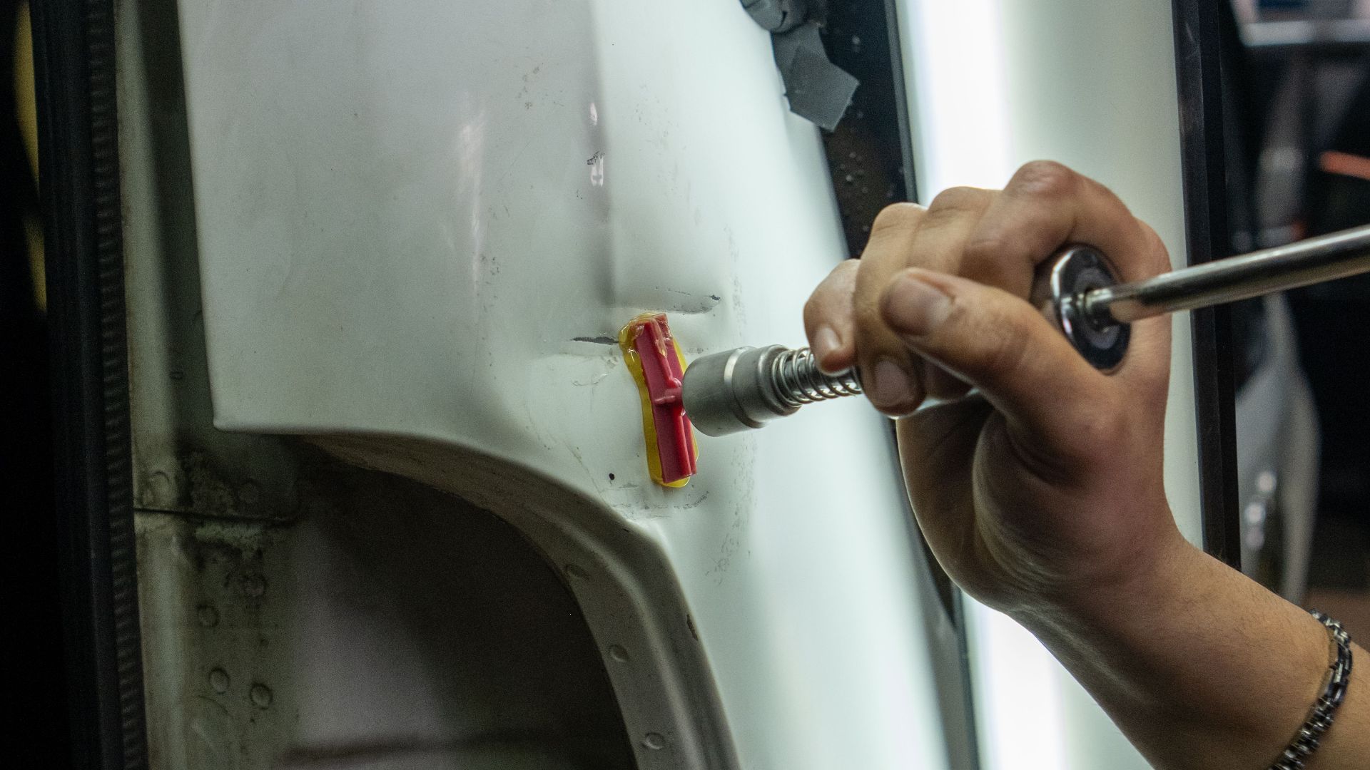 Close-up of vehicle dent repair in a garage using specialized tools under bright lighting.
