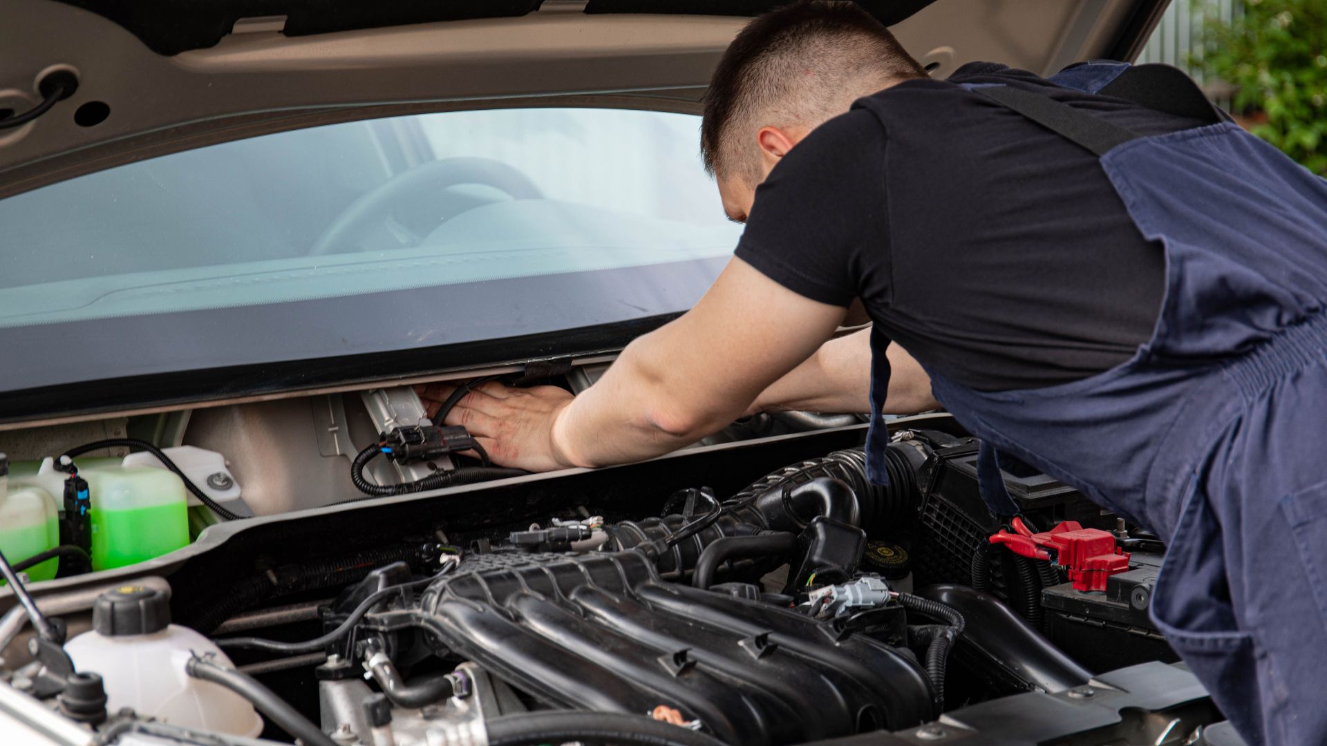 Auto mechanic performs engine maintenance on a car. Focus on hands and engine components.