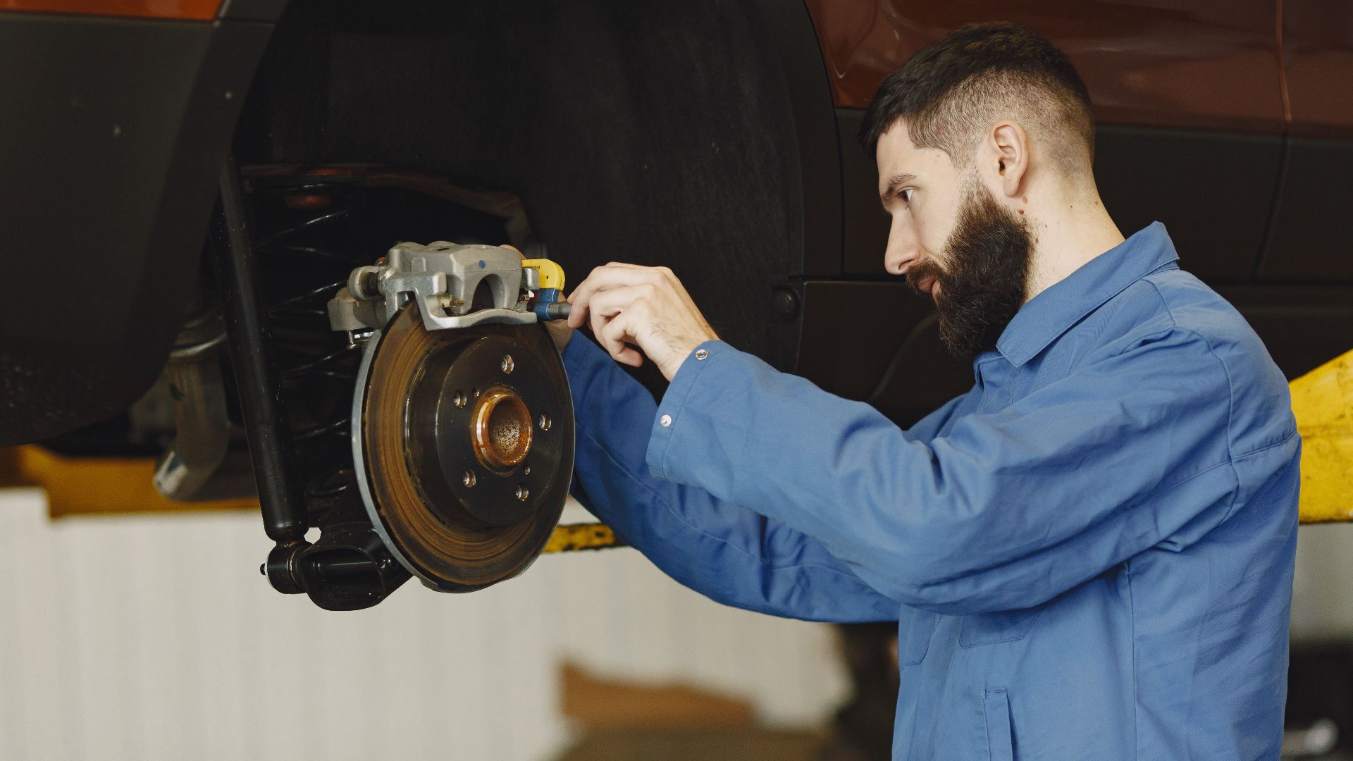 Mechanic in blue uniform performing brake repair on car in modern garage.