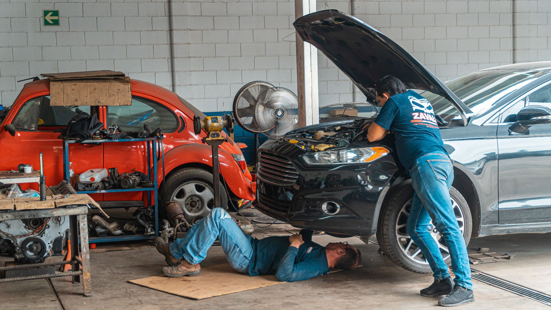 Mechanics working in an automotive workshop, repairing cars and performing maintenance.