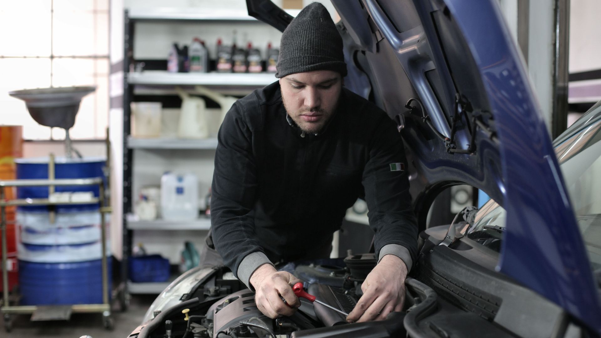 Man working under car hood in a garage, focused on engine repair