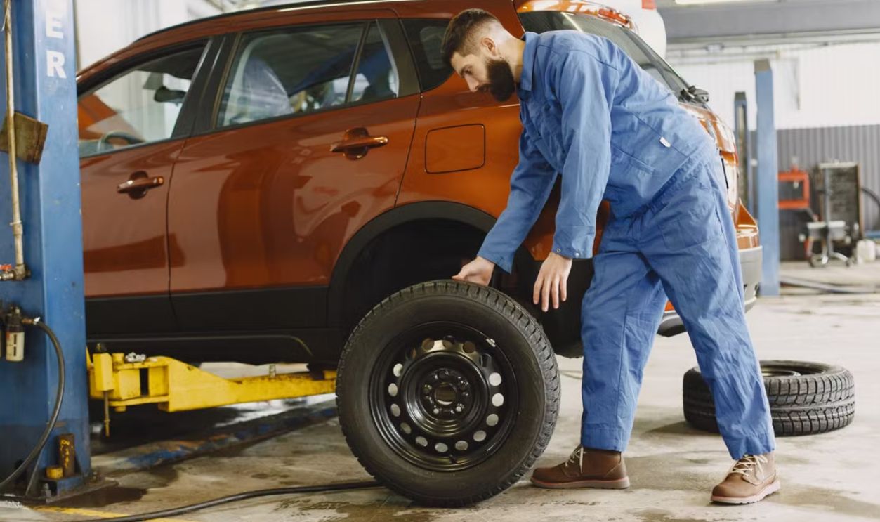 Mechanic in blue coveralls replacing tire on red SUV in repair shop garage